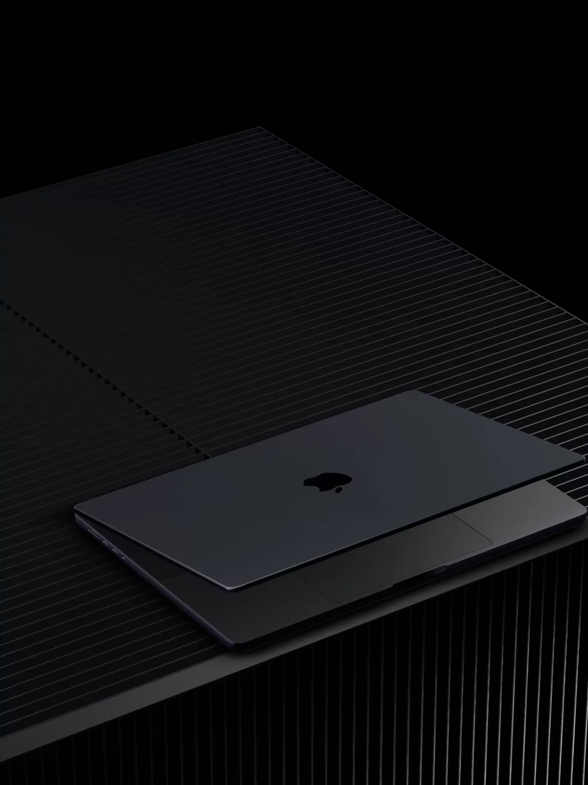 A closed laptop on a dark ridged surface, lit from one side.